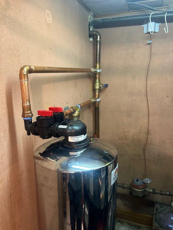 Completed installation of water filtration system with stainless steel tank and control valve assembly. System was properly connected to existing plumbing with copper piping and secured to wall with metal brackets. Also serviced water heater and verified proper connections to ensure complete household water treatment functionality.