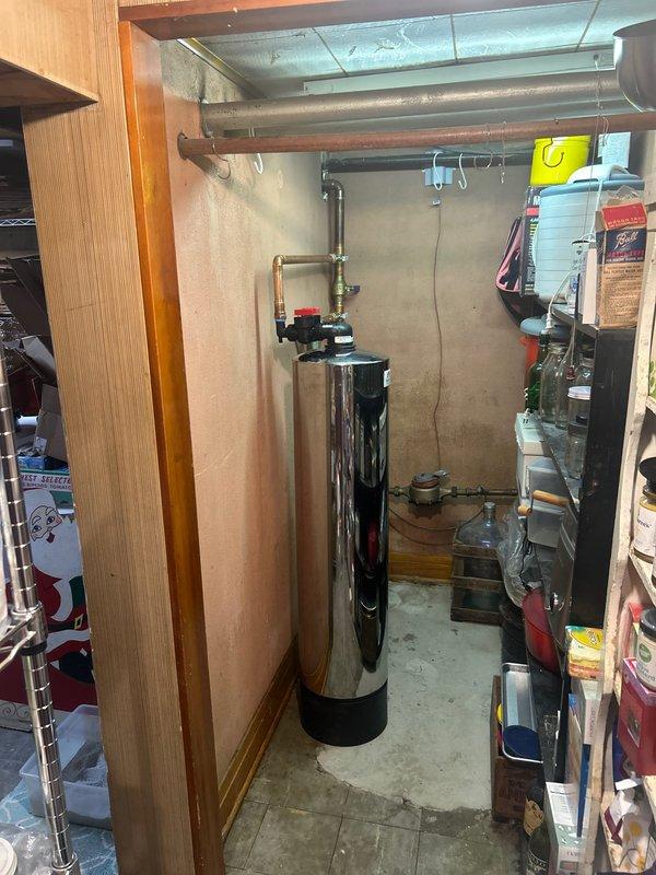 Completed installation of water filtration system with stainless steel tank and control valve assembly. System was properly connected to existing plumbing with copper piping and secured to wall with metal brackets. Also serviced water heater and verified proper connections to ensure complete household water treatment functionality.