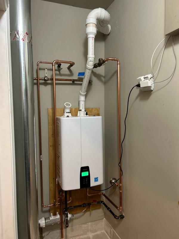 Successfully installed a new tankless water heater mounted on a wooden backing board with complete copper pipe network connections. System includes proper PVC venting, all necessary valves and fittings, and connection to the electrical control unit. Completed Energy Star certified installation with all components functioning properly.