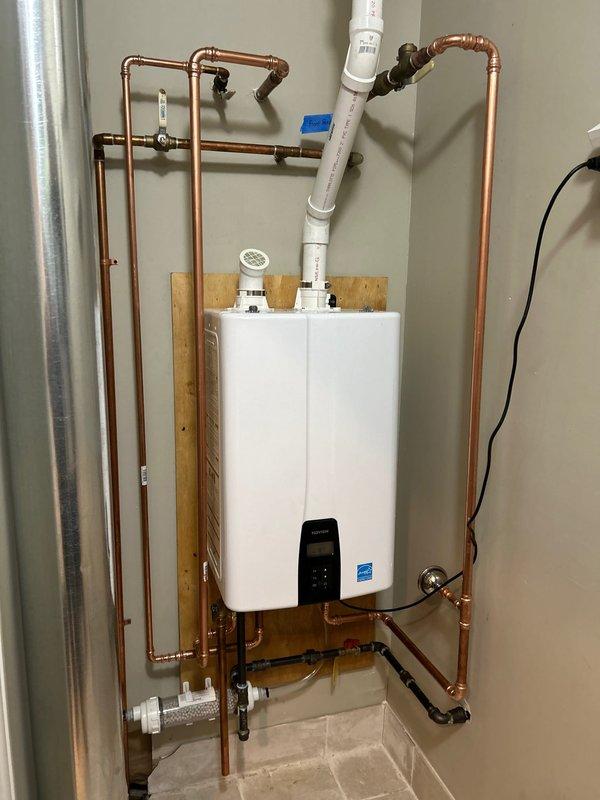 Successfully installed a new tankless water heater mounted on a wooden backing board with complete copper pipe network connections. System includes proper PVC venting, all necessary valves and fittings, and connection to the electrical control unit. Completed Energy Star certified installation with all components functioning properly.