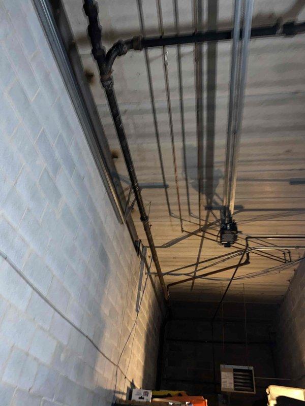 Conducted initial site assessment and photo documentation of basement drainage system and overhead plumbing infrastructure. Scheduled follow-up walkthrough with Kevin Grippo and Flynn to develop comprehensive material list for the upcoming project. Noted existing floor drain condition and ceiling pipe configuration for proper planning purposes.