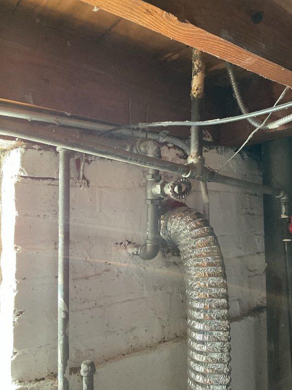 Inspected 10-year-old tank water heater and identified significant corrosion on the top water line connection. Documented condition with photos showing the installation environment including exposed plumbing infrastructure and surrounding utility area.
