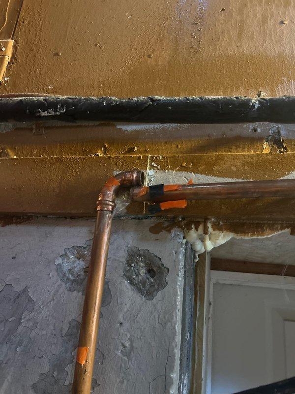 Conducted initial assessment of deteriorated plumbing system, identifying oxidized copper pipes with failing tape repairs and evidence of moisture damage to surrounding wall structures. Scheduled immediate follow-up service with additional technician for comprehensive pipe replacement and wall repair to address visible water damage and potential leakage points.