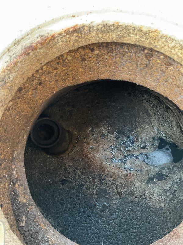 Successfully cleared main line blockage by rodding, and removed accumulated grease from catch basin. Visual inspection revealed significant pipe corrosion and rust buildup in the drainage system, with debris accumulation around the exterior drain cover.