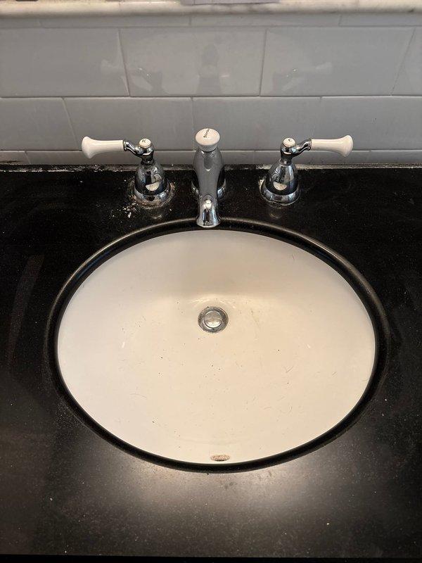 Completed bathroom sink installation with three-piece chrome faucet set on dark stone countertop. Installed new PVC P-trap drain assembly, connecting fixture to existing wall plumbing, ensuring proper drainage and leak-free operation.