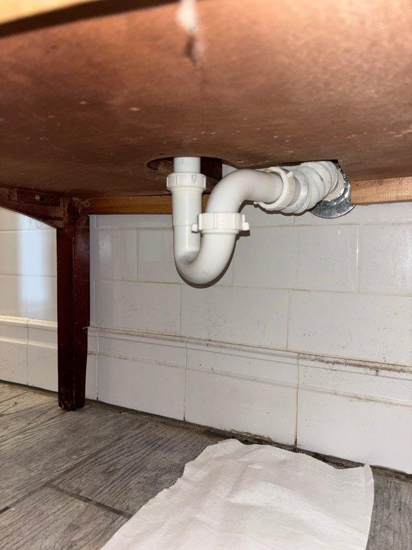 Completed bathroom sink installation with three-piece chrome faucet set on dark stone countertop. Installed new PVC P-trap drain assembly, connecting fixture to existing wall plumbing, ensuring proper drainage and leak-free operation.