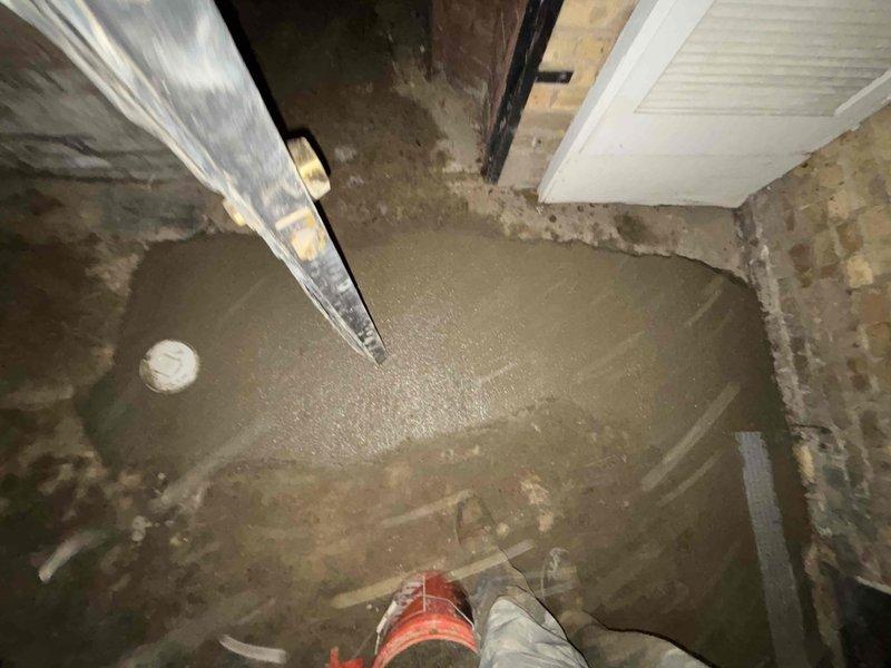 Completed concrete pour around new drainage system in basement/crawl space. Installed PVC drain pipe with proper 90-degree angle configuration and connected to drainage grate. Excavated and prepared area for proper drainage flow and finished with fresh concrete surface.