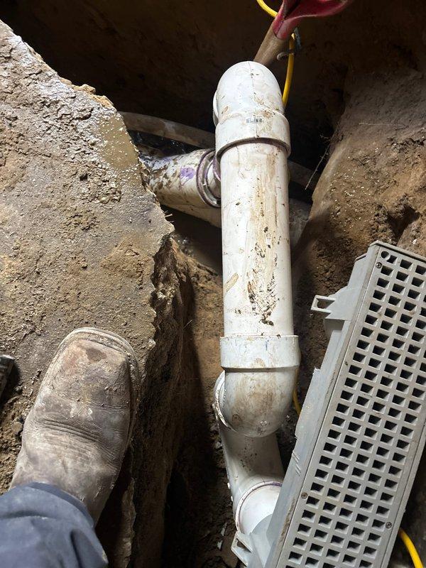 Completed concrete pour around new drainage system in basement/crawl space. Installed PVC drain pipe with proper 90-degree angle configuration and connected to drainage grate. Excavated and prepared area for proper drainage flow and finished with fresh concrete surface.