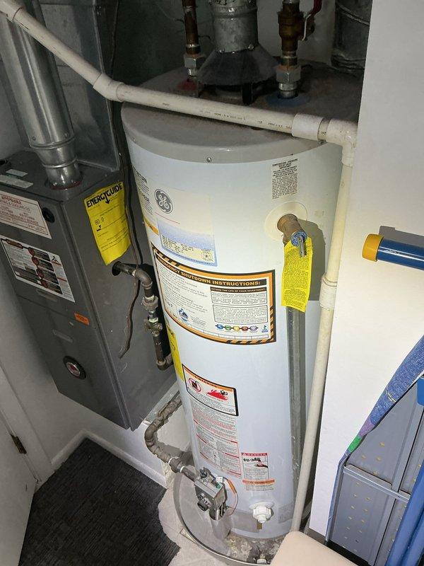 Inspected 16-year-old GE 40-gallon water heater showing active leakage from tank bottom that customer reported began several months ago. Observed significant rust and corrosion on galvanized steel pipes and fittings, particularly at elbow joints. Recommended complete replacement of water heater due to age and deteriorating condition of tank and connection components.