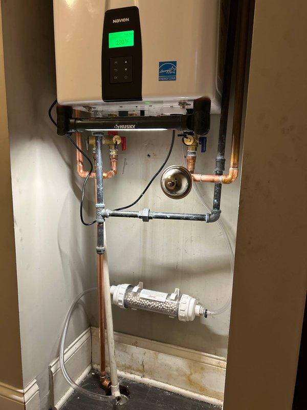 Successfully installed a Navien wall-mounted water heater in utility area. Installation included complete copper and PVC piping connections, valve installations, and a sediment filter mounting. System was properly configured with temperature settings and all connections were verified for proper operation.