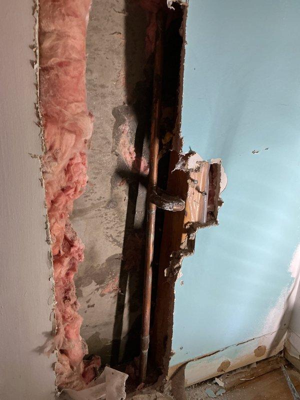 Located and assessed burst copper pipes within wall cavity. Cut access opening to expose damaged section, revealing water damage to surrounding insulation and drywall. Repaired burst pipe section and verified system integrity before closing.