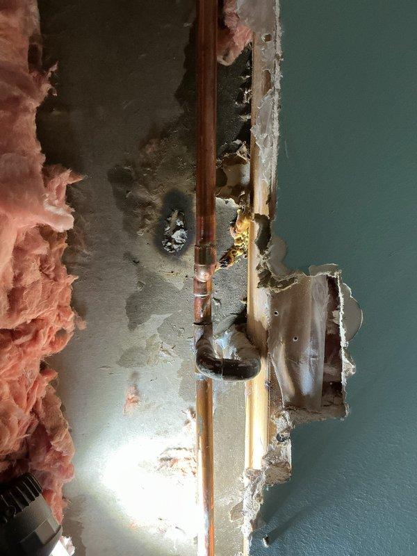 Located and assessed burst copper pipes within wall cavity. Cut access opening to expose damaged section, revealing water damage to surrounding insulation and drywall. Repaired burst pipe section and verified system integrity before closing.