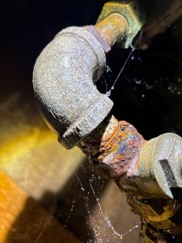 Responded to emergency call for burst pipe. Upon inspection, discovered heavily corroded elbow joint with active water leakage in wall access panel. Replaced deteriorated pipe fitting to resolve the leak and prevent further water damage.