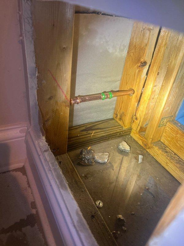 Responded to emergency call regarding frozen pipe behind toilet. Upon inspection, discovered water intrusion with approximately 1" of standing water at the base of the wall. Created access point in wall to expose affected copper supply line with visible frost damage. Thawed pipe, verified proper water flow, and inspected for leaks before recommending additional insulation for exposed plumbing in this area to prevent future freezing issues.