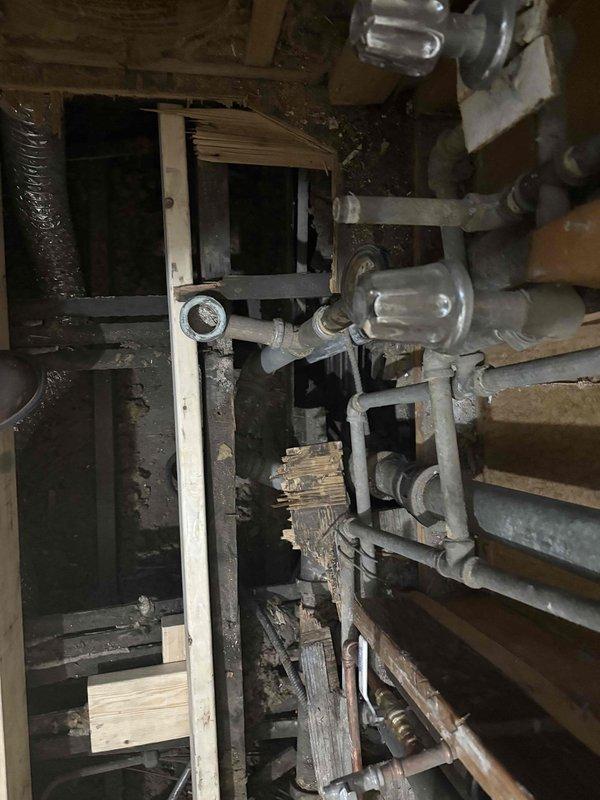 Inspected existing water heater system to provide replacement estimate. Observed significant corrosion and rust damage on vertical supply pipe, as well as deterioration in surrounding plumbing infrastructure. Identified potential water damage in utility area and documented current system configuration including pipe connections and flow indicators for accurate replacement specifications.