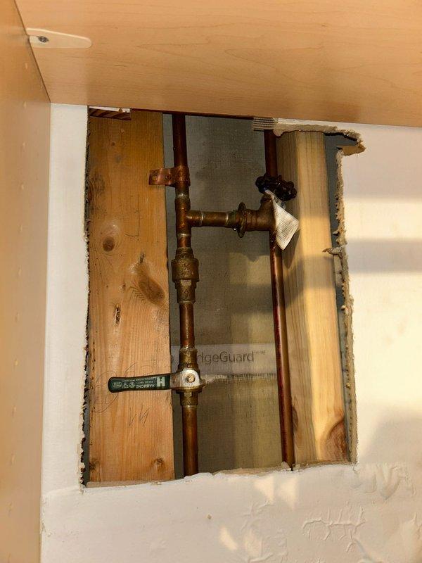 Responded to emergency call for burst pipe in kitchen. Upon inspection, identified a significant water leak from a copper supply line with visible crack and mineral buildup. Cut access panel in wall to expose plumbing components, isolated water supply using valve controls, and replaced damaged section of copper pipe including T-junction and associated brass fittings.