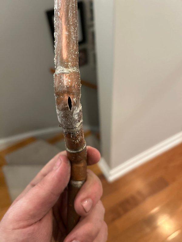 Responded to emergency call for burst pipe in kitchen. Upon inspection, identified a significant water leak from a copper supply line with visible crack and mineral buildup. Cut access panel in wall to expose plumbing components, isolated water supply using valve controls, and replaced damaged section of copper pipe including T-junction and associated brass fittings.