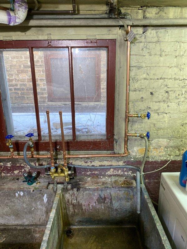 Completed copper plumbing work on utility sink system in basement. Installed new shutoff valves with blue handles and replaced deteriorated copper pipe sections. Ensured proper connection to concrete dual-basin utility sink and tested for leaks.