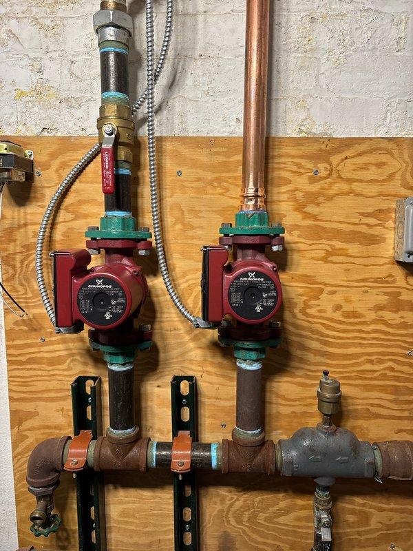 Successfully collected down payment for plumbing repair job sold by Nick B. Documentation includes photos of the existing copper pipe infrastructure in the utility area and the dual red circulation pumps with green flanges mounted on plywood, which will be addressed during the scheduled repair work.