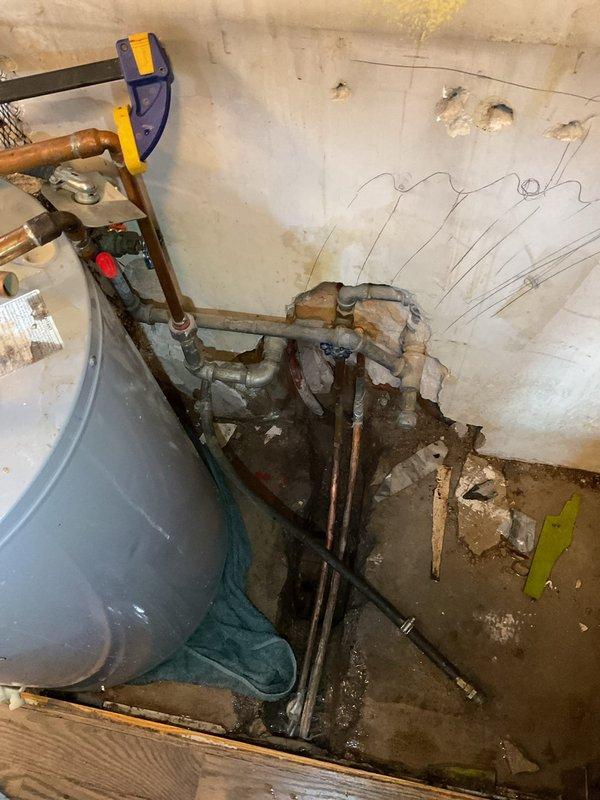 Responded to emergency call for water backing up through floor. Upon inspection, discovered significant water leak in utility room with previous technician having removed water heater. Diagnosed issue as deteriorated copper supply lines with visible corrosion causing water intrusion into wall and floor. Replaced damaged plumbing connections, restored water service, and verified system functionality with no further leakage.