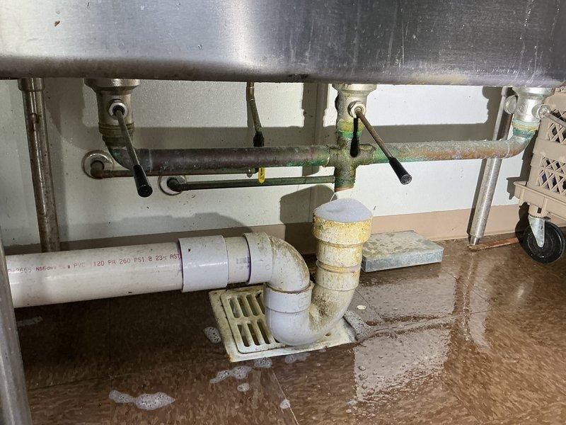 Performed comprehensive assessment of commercial plumbing system requiring multiple repairs. Evaluated failing sump pump requiring replacement, identified deteriorated PVC drainage pipes with mineral deposits and leakage issues. Documented necessary repairs including reconfiguration of kitchen P-trap, correction of women's bathroom hot water valve malfunction, and sealing of leaking ground drainage pipe connection.