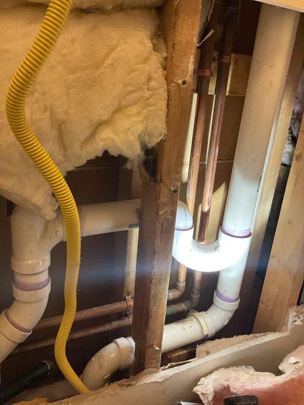 Completed assessment of exposed wall plumbing system, inspecting PVC drainage pipes, water supply connections with hot/cold valves, and associated gas line. Documented current installation configuration including U-shaped drain assembly and utility box placement for commercial drain and sewer estimate.