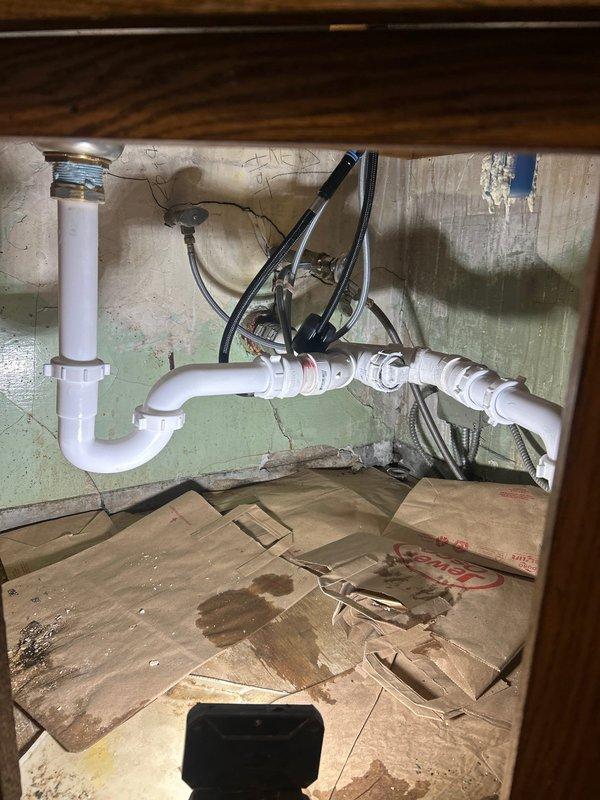 Completed plumbing repair job under sink, replacing damaged P-trap assembly and drain pipe connections. Addressed visible water damage and moisture issues, installing new PVC drainage components with proper seals at all connection points. All supply lines were secured and tested for proper drainage functionality.