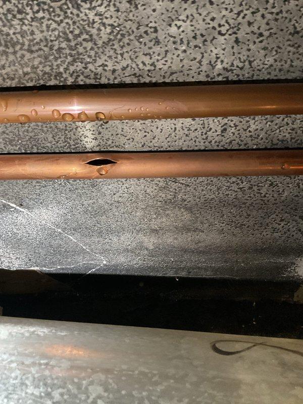 Responded to a service call for a burst copper pipe. Inspection revealed a horizontal supply line with a significant longitudinal split and another pipe showing signs of condensation. Water damage was evident on surrounding drywall and ceiling materials. Replaced the damaged section of pipe and checked adjacent plumbing components for potential secondary failures.