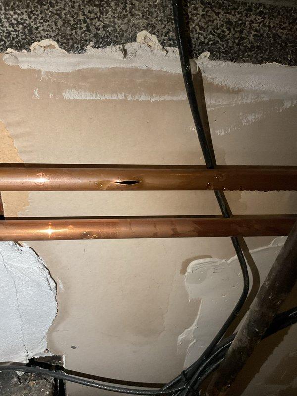 Responded to a service call for a burst copper pipe. Inspection revealed a horizontal supply line with a significant longitudinal split and another pipe showing signs of condensation. Water damage was evident on surrounding drywall and ceiling materials. Replaced the damaged section of pipe and checked adjacent plumbing components for potential secondary failures.