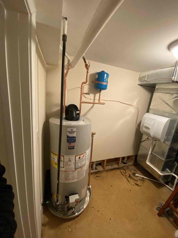 Completed installation of new water heater system with copper piping connections, including a pressure regulator and expansion tank mounted to the wall. System was properly fitted with necessary valves and connected to existing PVC discharge lines.