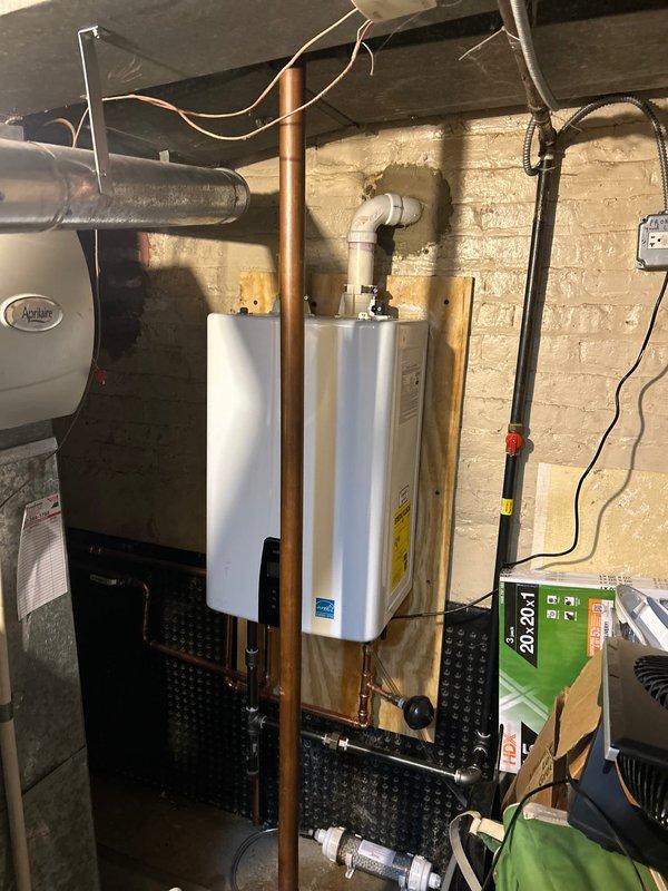 Successfully installed new Energy Star rated tankless water heater on brick wall in utility area, connecting all necessary copper and PVC piping. Completed exterior wall penetration with PVC vent pipe, properly sealed around brick opening for code compliance and optimal system ventilation.