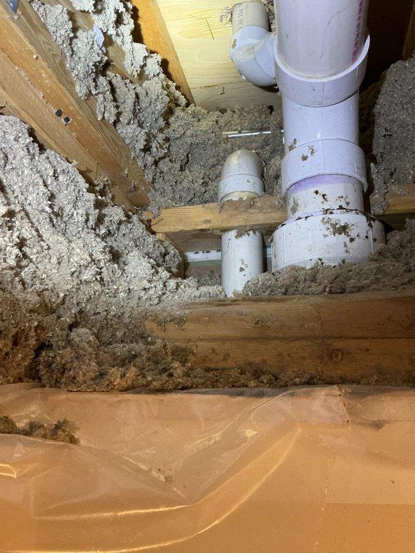 Responded to a water leak complaint where upstairs bathroom sink usage was causing water intrusion in the lower unit's bedroom closet. Inspected the plumbing system between units and identified water infiltration pathways. Examined PVC drainage pipes and connections within the joist space, noting disturbed insulation around the plumbing. Leak source was documented with photographic evidence showing the affected drainage system and surrounding structural elements.