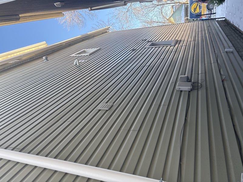 Completed installation of tankless water heater as sold by Jon. Documentation includes exterior photos of building structure and metal roofing with proper ventilation penetrations in place.