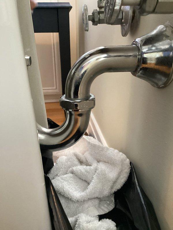 Located and repaired two leaks in bathroom sink plumbing: tightened loose connection on chrome P-trap J-bend and replaced faulty hot water angle stop valve. Tested all connections to confirm proper function with no further dripping observed.