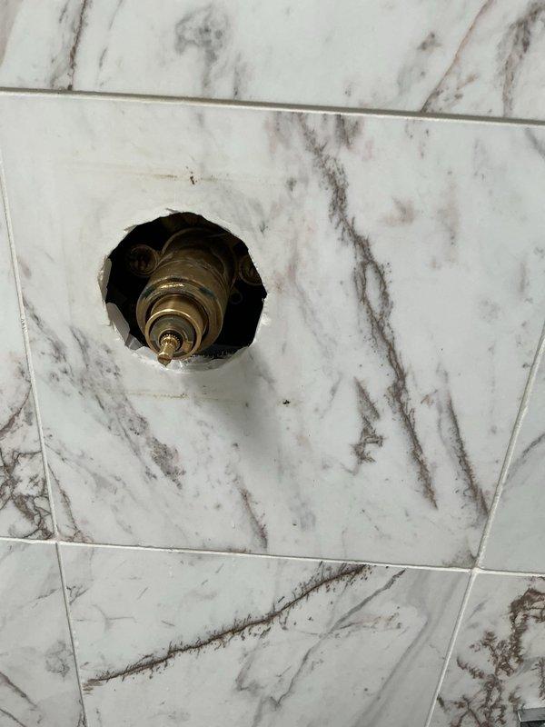Responded to a building shut down service call to repair a shower valve assembly. Upon inspection, found the existing brass valve showing signs of mineral buildup and discoloration. Successfully removed the damaged components and installed a new valve assembly in the marble-tiled wall, ensuring proper function before completing the service.