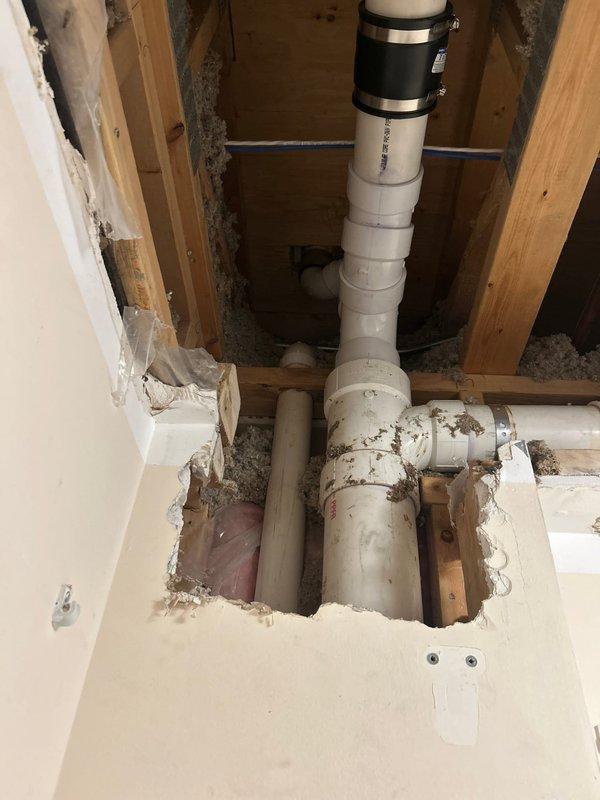 Completed sold repair job originally sold by Brian R. Accessed residential drainage system through opened wall section, replacing damaged PVC piping in the stack and horizontal runs. Installed new black rubber couplings with metal clamps to secure connections, ensuring proper drainage function through the wooden framing structure.