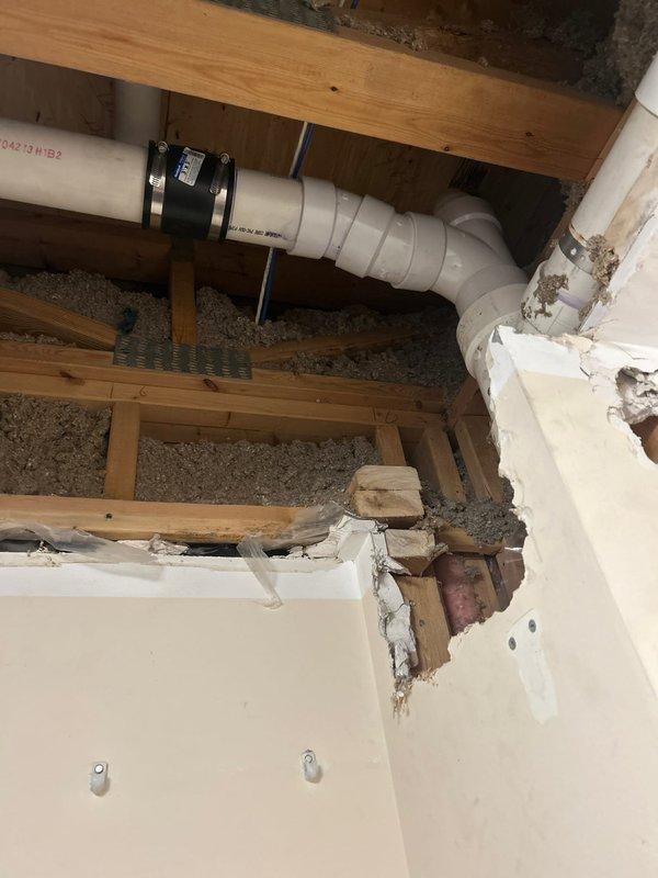 Completed sold repair job originally sold by Brian R. Accessed residential drainage system through opened wall section, replacing damaged PVC piping in the stack and horizontal runs. Installed new black rubber couplings with metal clamps to secure connections, ensuring proper drainage function through the wooden framing structure.