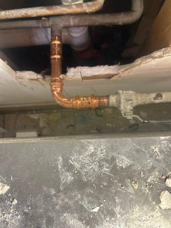 Responded to emergency service call for burst pipe in laundry room area. Upon inspection, discovered a split copper pipe with significant frost buildup at a curved section. Water supply was already shut off by customer. Accessed the affected plumbing through wall cavity, replaced damaged copper section with new pipe and fittings, and reconnected to existing PVC line. Tested system for leaks after repair and restored water service.