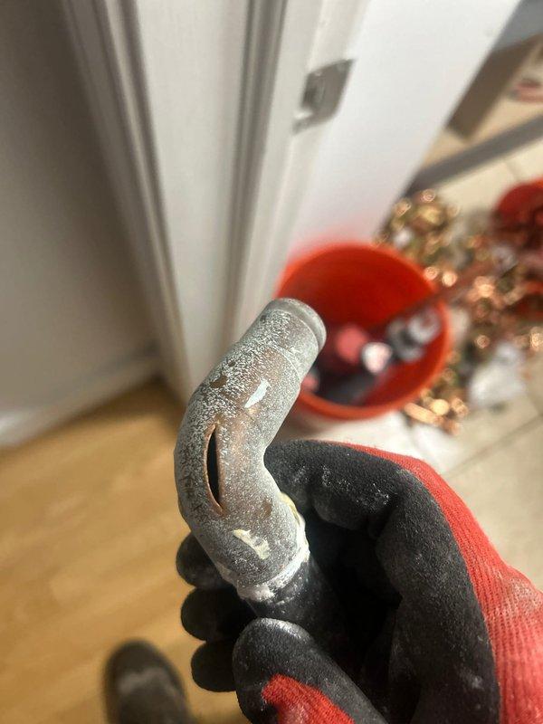 Responded to emergency service call for burst pipe in laundry room area. Upon inspection, discovered a split copper pipe with significant frost buildup at a curved section. Water supply was already shut off by customer. Accessed the affected plumbing through wall cavity, replaced damaged copper section with new pipe and fittings, and reconnected to existing PVC line. Tested system for leaks after repair and restored water service.
