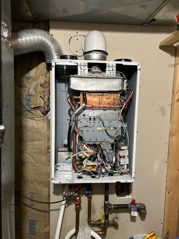 Responded to customer complaint of leakage from tankless water heater unit. Performed diagnostic inspection after customer reported water continuously running through heat exchanger. Opened front panel to examine internal components, revealing oxidation on copper components and inspected all connections for source of leakage. Placed collection bucket below unit to contain water during service inspection.