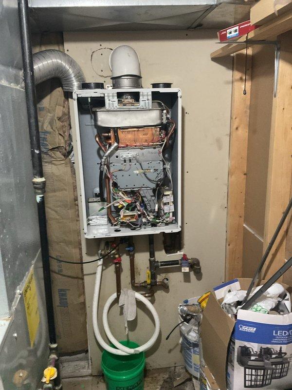Responded to customer complaint of leakage from tankless water heater unit. Performed diagnostic inspection after customer reported water continuously running through heat exchanger. Opened front panel to examine internal components, revealing oxidation on copper components and inspected all connections for source of leakage. Placed collection bucket below unit to contain water during service inspection.