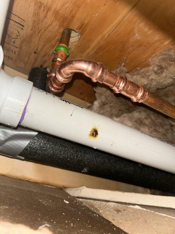 Responded to emergency call for a burst pipe in ceiling/wall cavity. Located and replaced damaged copper pipe section showing significant leakage, as evidenced by water staining on adjacent PVC pipe and surrounding materials. Installed new copper pipe with proper fittings and verified system integrity with pressure test after repair.