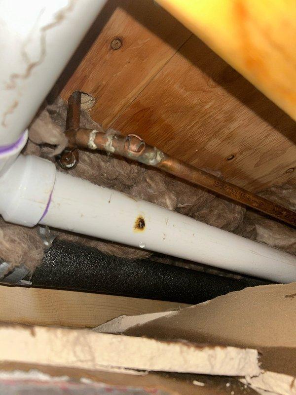 Responded to emergency call for a burst pipe in ceiling/wall cavity. Located and replaced damaged copper pipe section showing significant leakage, as evidenced by water staining on adjacent PVC pipe and surrounding materials. Installed new copper pipe with proper fittings and verified system integrity with pressure test after repair.