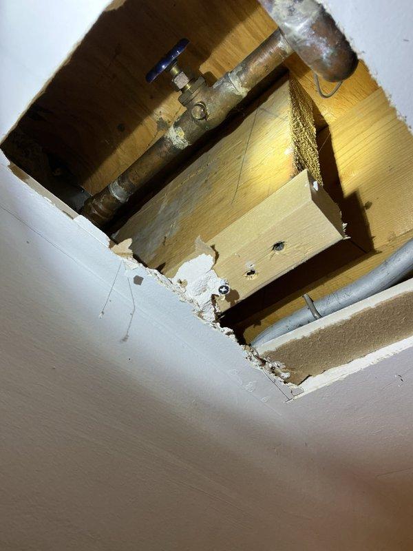 Located and inspected water leak in garage ceiling that had begun during the weekend. Upon investigation, accessed the affected area by creating a ceiling cutout, revealing copper water supply lines with visible corrosion and a deteriorated brass shutoff valve. Identified this as the source of the leak.