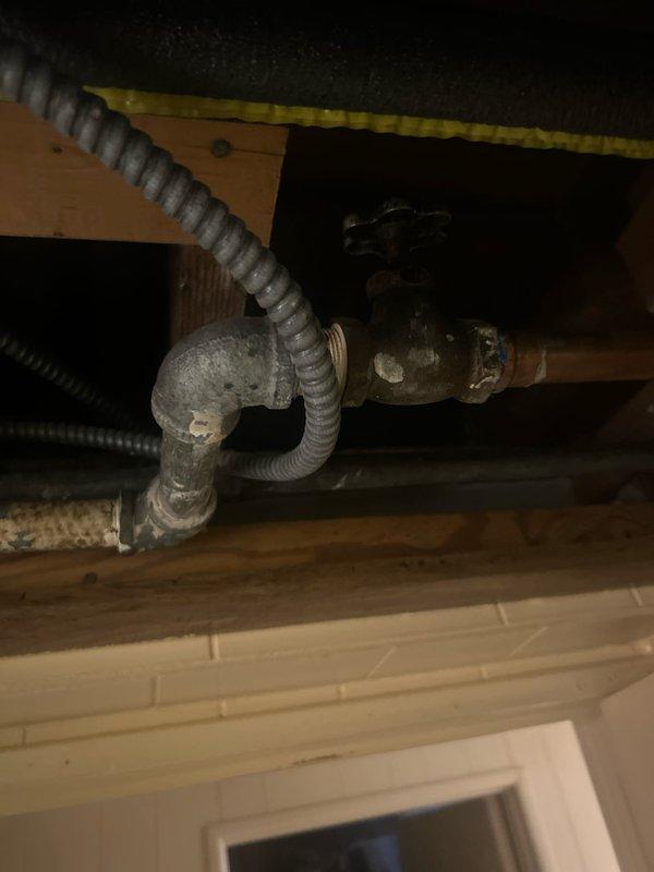 Located and identified water leak source in basement, originating from a corroded metal pipe with deteriorating elbow joint. Accessed the affected area by creating an inspection opening in the wall structure, revealing aged plumbing components with visible wear and discoloration requiring attention.
