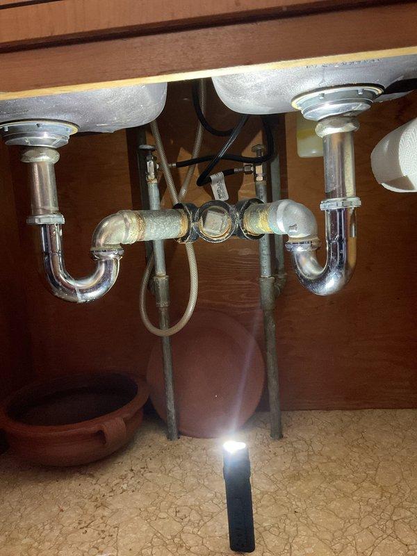Responded to service call for kitchen double-basin sink with slow drainage. Visual inspection revealed standard P-trap configuration with horizontal connection pipe between drains. Successfully cleared clog and restored normal drainage function in both basins.