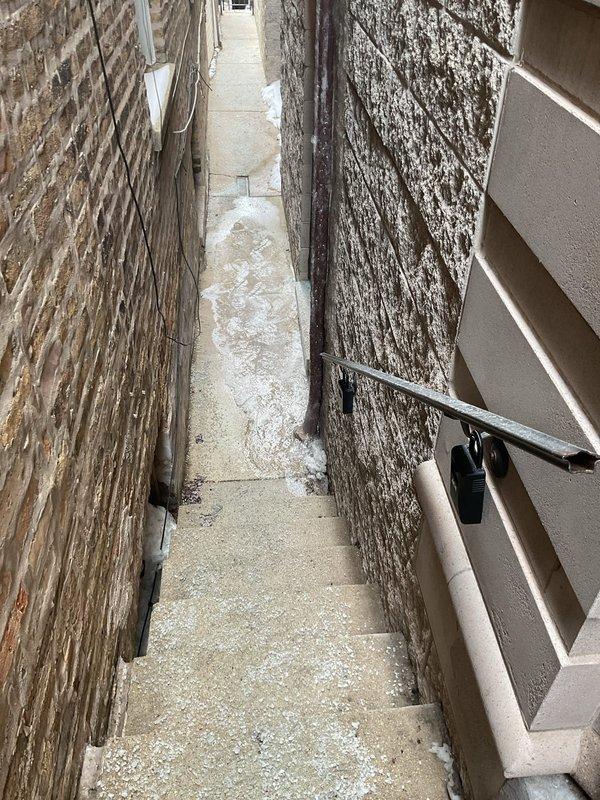 Conducted site inspection of narrow alleyway between two buildings where gutters are freezing and causing sewer backup issues outside. Documented the affected area including the drainage pathway and building exterior features. Customer was not present during assessment.