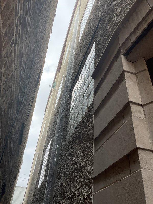 Conducted site inspection of narrow alleyway between two buildings where gutters are freezing and causing sewer backup issues outside. Documented the affected area including the drainage pathway and building exterior features. Customer was not present during assessment.