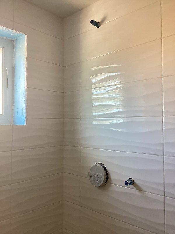 Conducted follow-up service visit as scheduled with client to evaluate bathroom renovation progress. Inspected newly installed white ceramic tile shower enclosure with mounted control valve and water supply lines. Noted copper pipe stub protruding from wall and verified floor drain installation (currently protected with temporary covering) in hexagonal tile flooring. Site appears to be in mid-installation phase requiring completion of fixture connections.