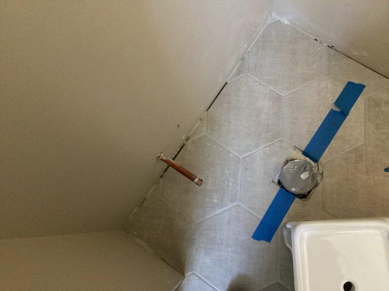 Conducted follow-up service visit as scheduled with client to evaluate bathroom renovation progress. Inspected newly installed white ceramic tile shower enclosure with mounted control valve and water supply lines. Noted copper pipe stub protruding from wall and verified floor drain installation (currently protected with temporary covering) in hexagonal tile flooring. Site appears to be in mid-installation phase requiring completion of fixture connections.